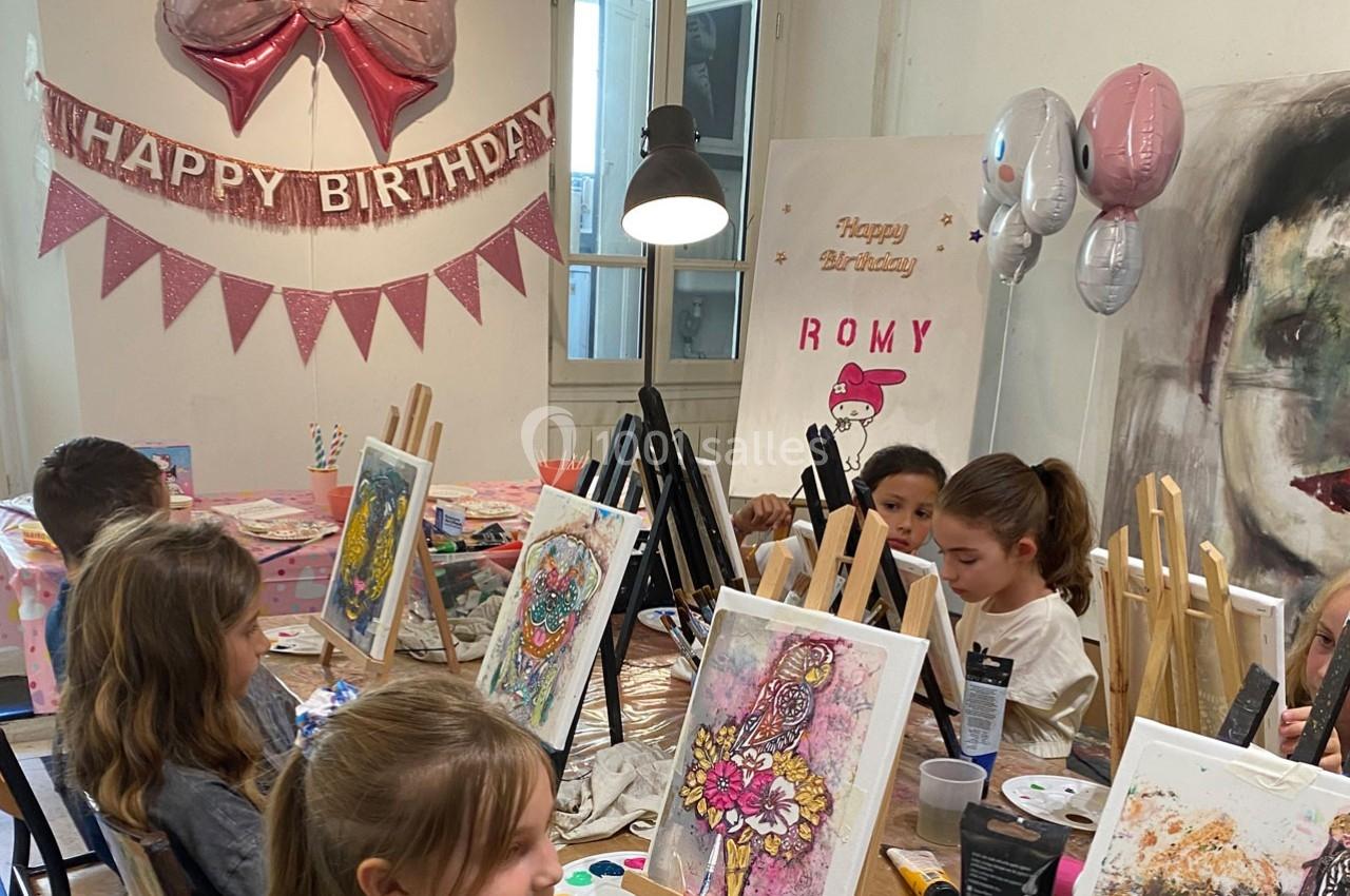 Des enfants peignent sur des chevalets lors d'une fête d'anniversaire décorée de ballons et de guirlandes.