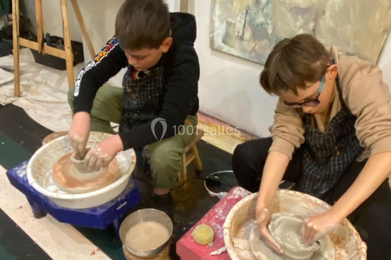 Deux enfants façonnent de l'argile sur des tours de potier dans un atelier artistique.