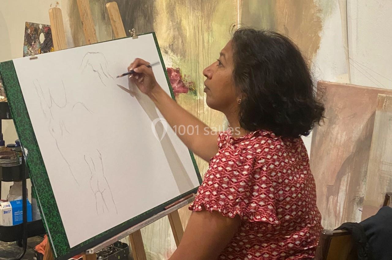 Une femme dessine sur une toile blanche posée sur un chevalet dans un atelier d'art.