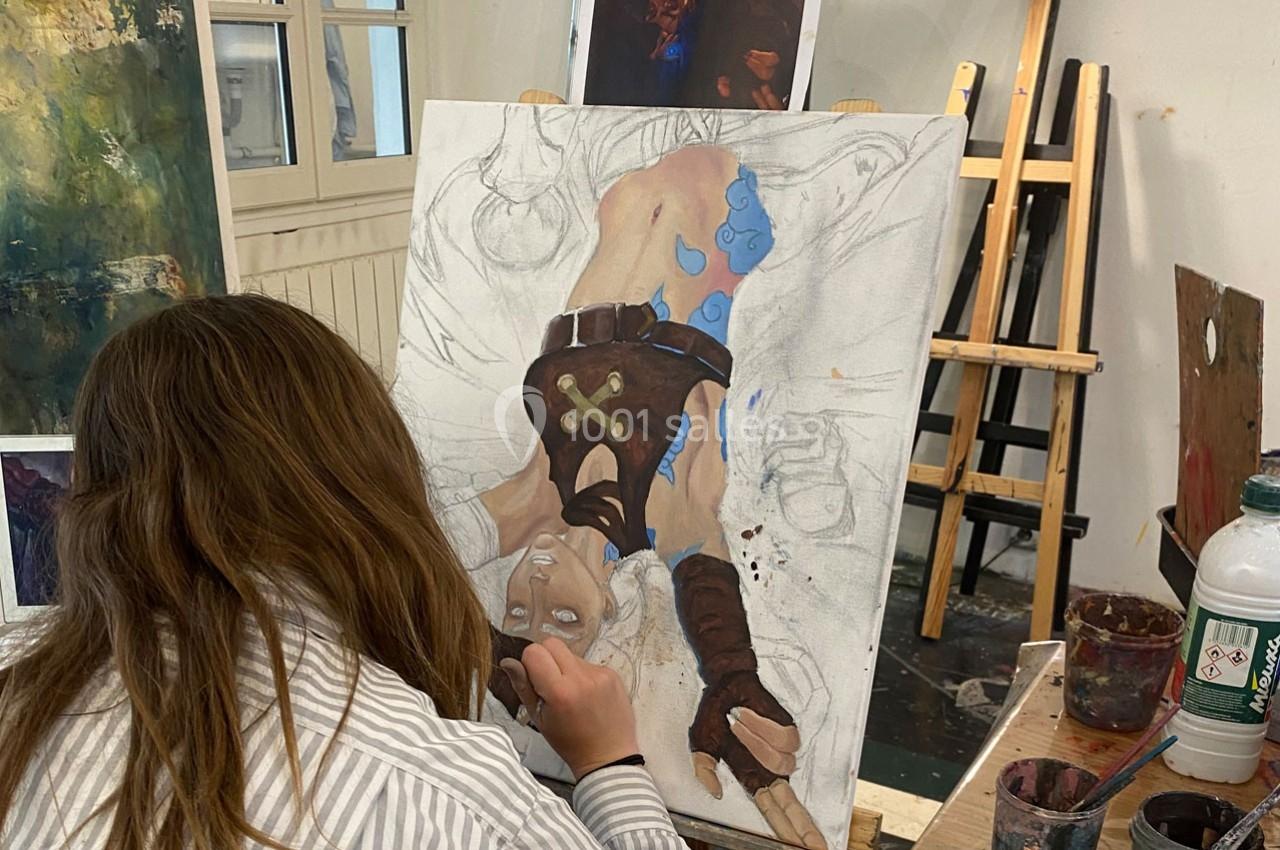 Une artiste peint une illustration détaillée d'un personnage fantastique sur une toile dans un atelier lumineux.