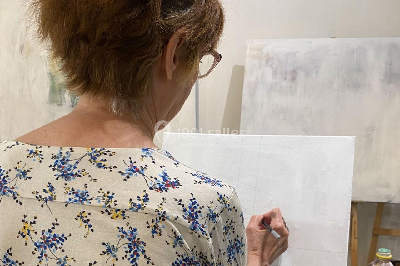 Femme de dos, dessinant sur une toile blanche dans un atelier lumineux.