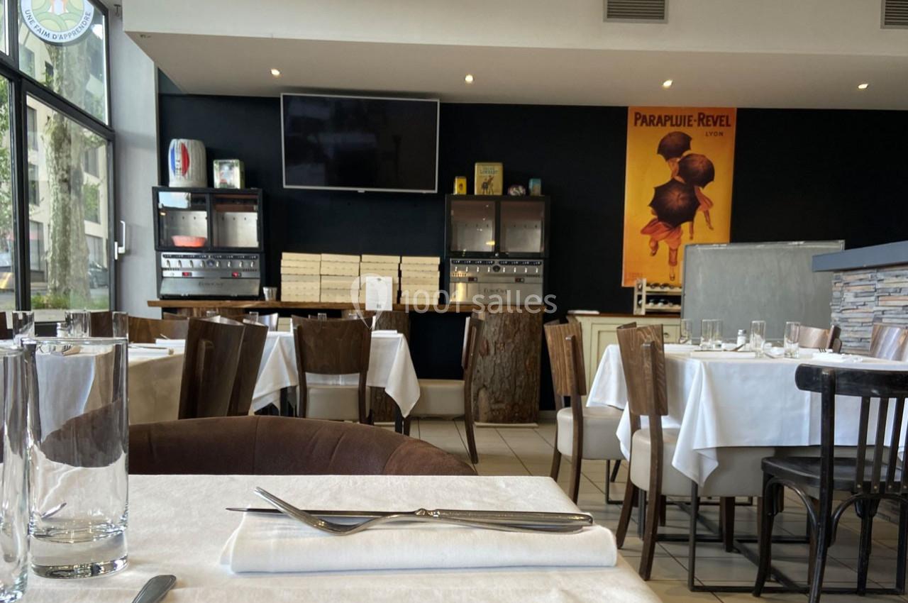 Salle de restaurant lumineuse avec tables dressées, chaises en bois, et décoration rétro sur un mur sombre.
