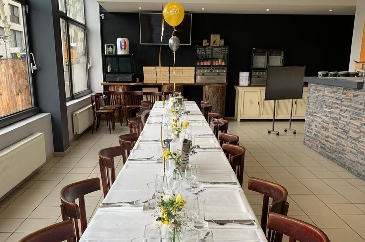 Table dressée avec nappes blanches, couverts et décorations florales, dans une salle lumineuse avec ballon ’60’.