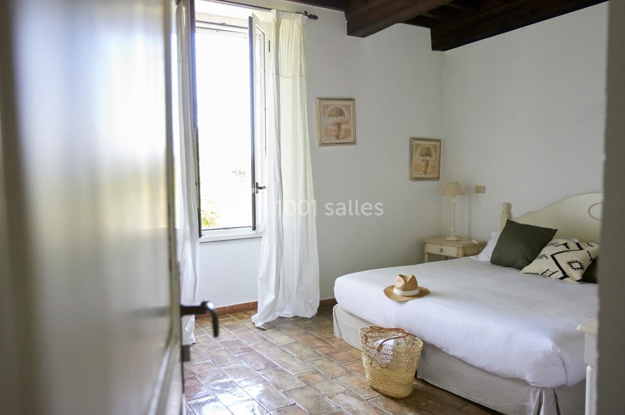 Chambre lumineuse avec lit double, fenêtre ouverte sur l'extérieur, sol en carreaux et décoration sobre.