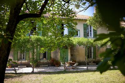 Vue d'une chambre cosy avec lit, éclairage doux, rideaux verts et table extérieure ornée de plantes et d'une tasse.