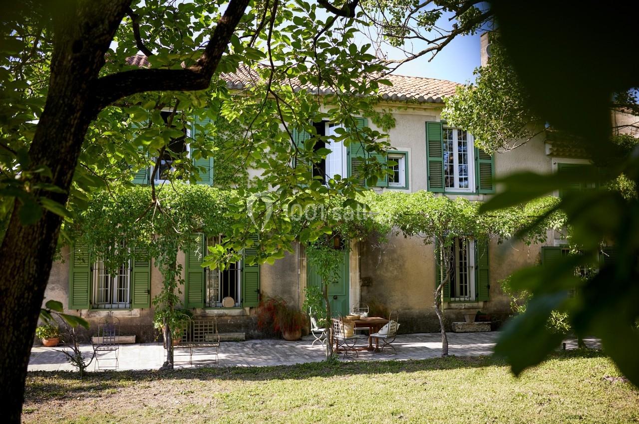 Façade d'une maison provençale avec volets verts, terrasse ombragée et végétation environnante.