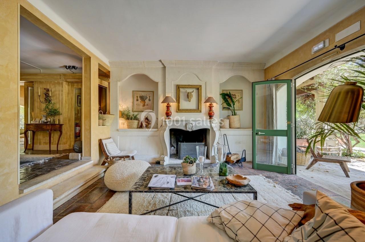 Salon lumineux avec cheminée, mobilier confortable, décor chaleureux et vue sur un jardin verdoyant par une porte ouverte.