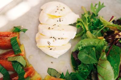 Vue d'une chambre cosy avec lit, éclairage doux, rideaux verts et table extérieure ornée de plantes et d'une tasse.