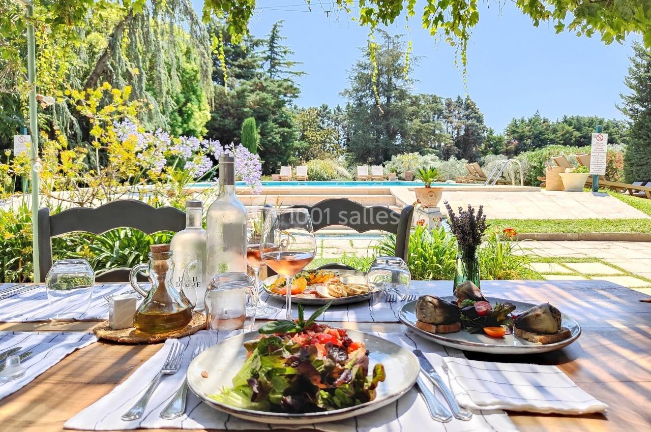 Table dressée en extérieur avec des assiettes de plats variés, vue sur un jardin verdoyant et une piscine en arrière-plan.