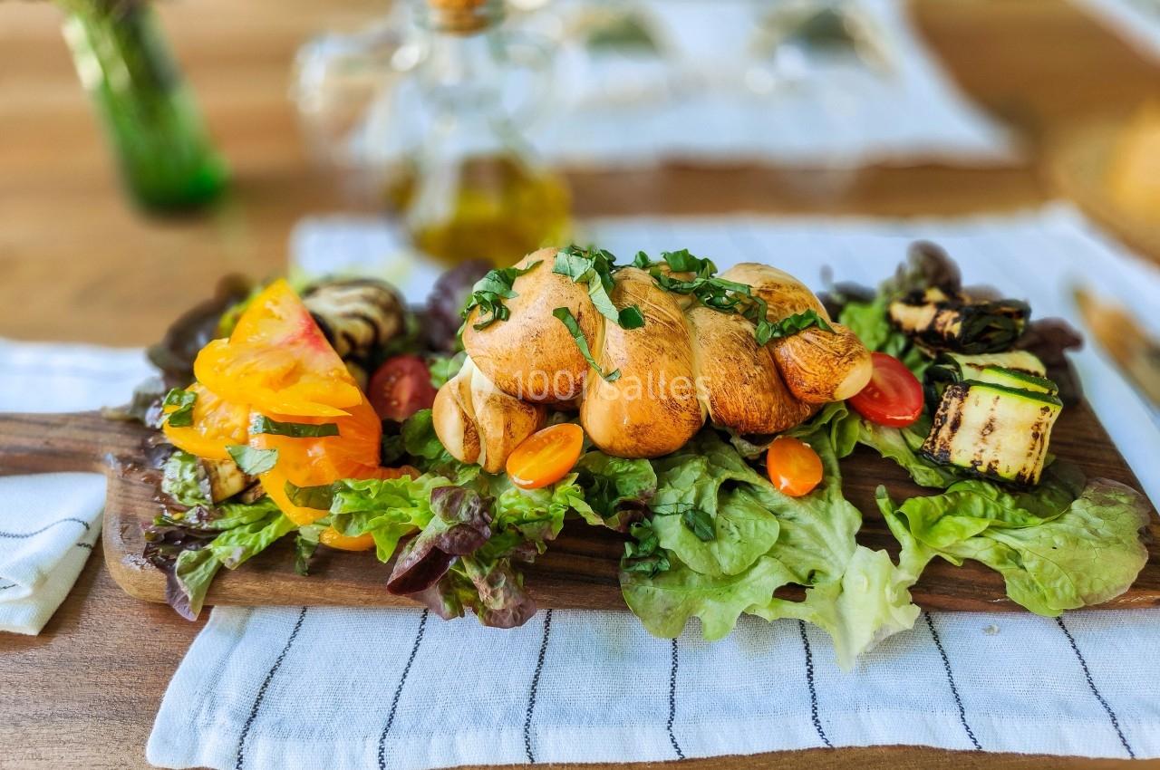 Assiette de légumes grillés et salade, accompagnée de pain torsadé, servie sur une planche en bois.