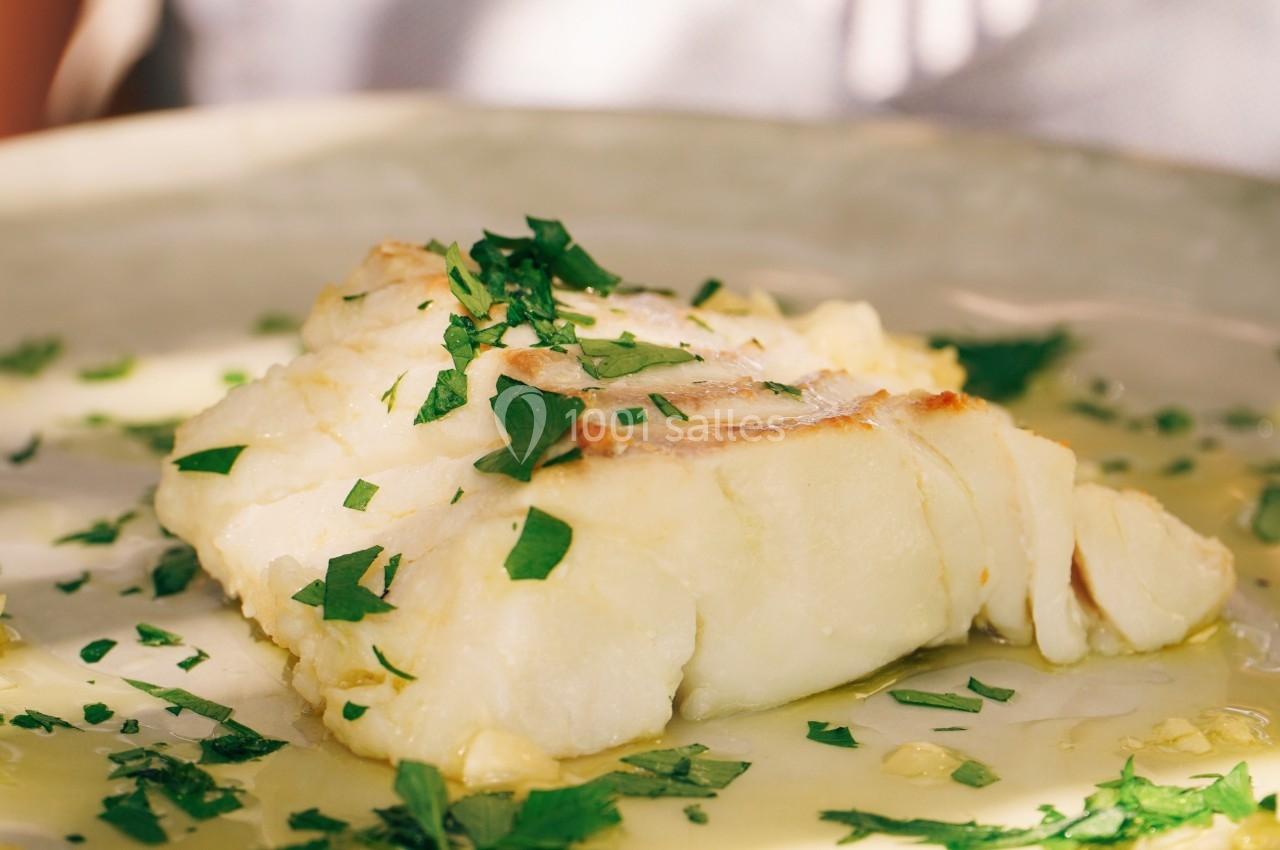 Filet de poisson blanc servi avec une sauce au beurre et parsemé de persil frais sur une assiette en céramique.