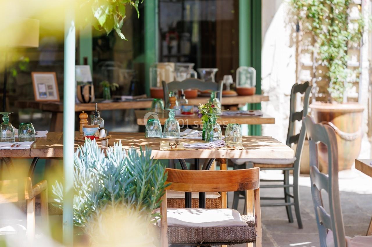 Terrasse d'un restaurant avec tables en bois dressées, entourées de plantes et baignée de lumière naturelle.