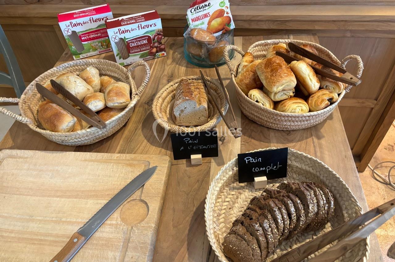 Buffet de petits-déjeuners avec paniers de viennoiseries, pains variés, couteaux et planche en bois.