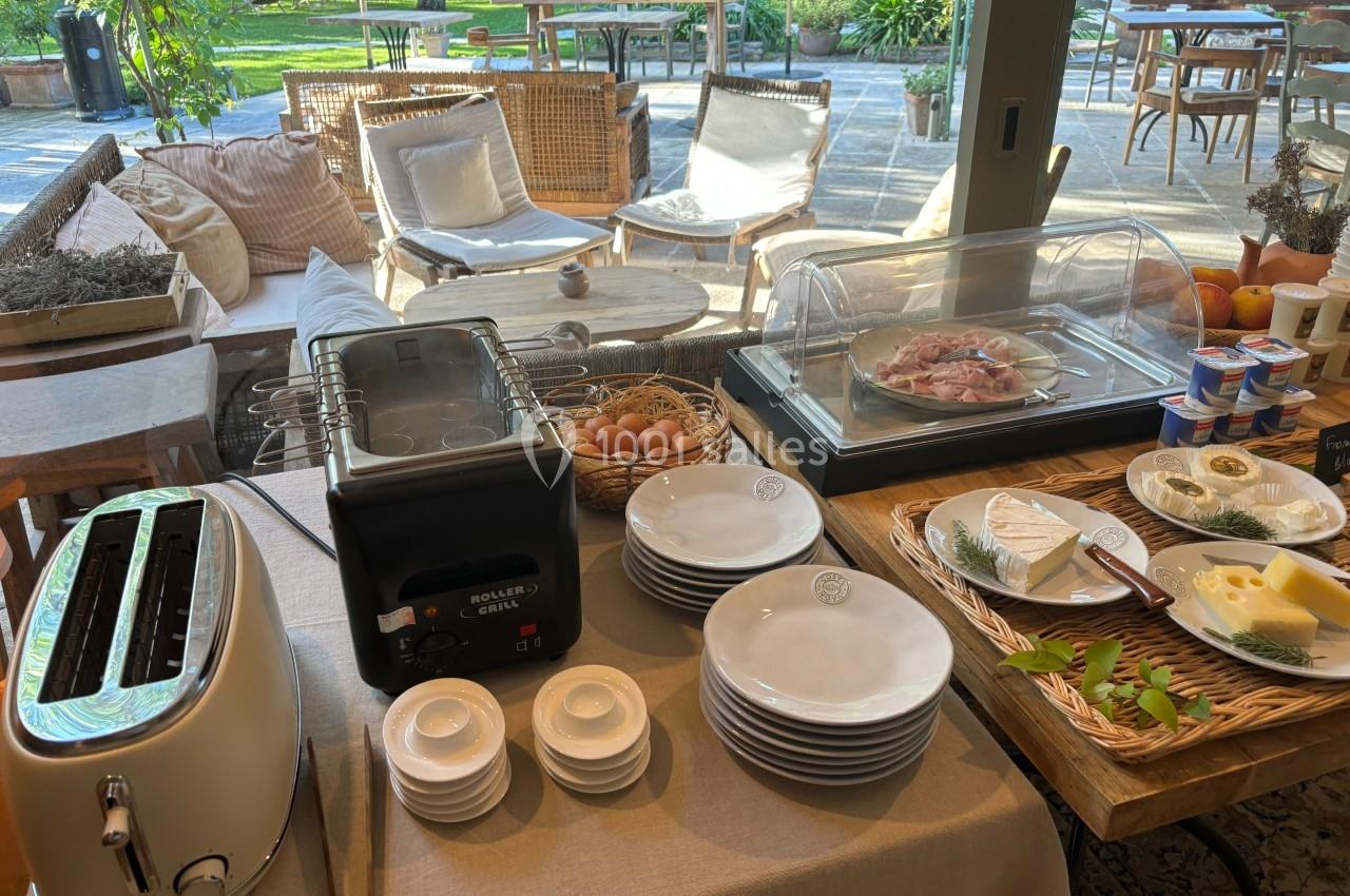 Buffet de petit-déjeuner avec grille-pain, œufs, charcuterie, fromages, yaourts et vaisselle dans un cadre lumineux.