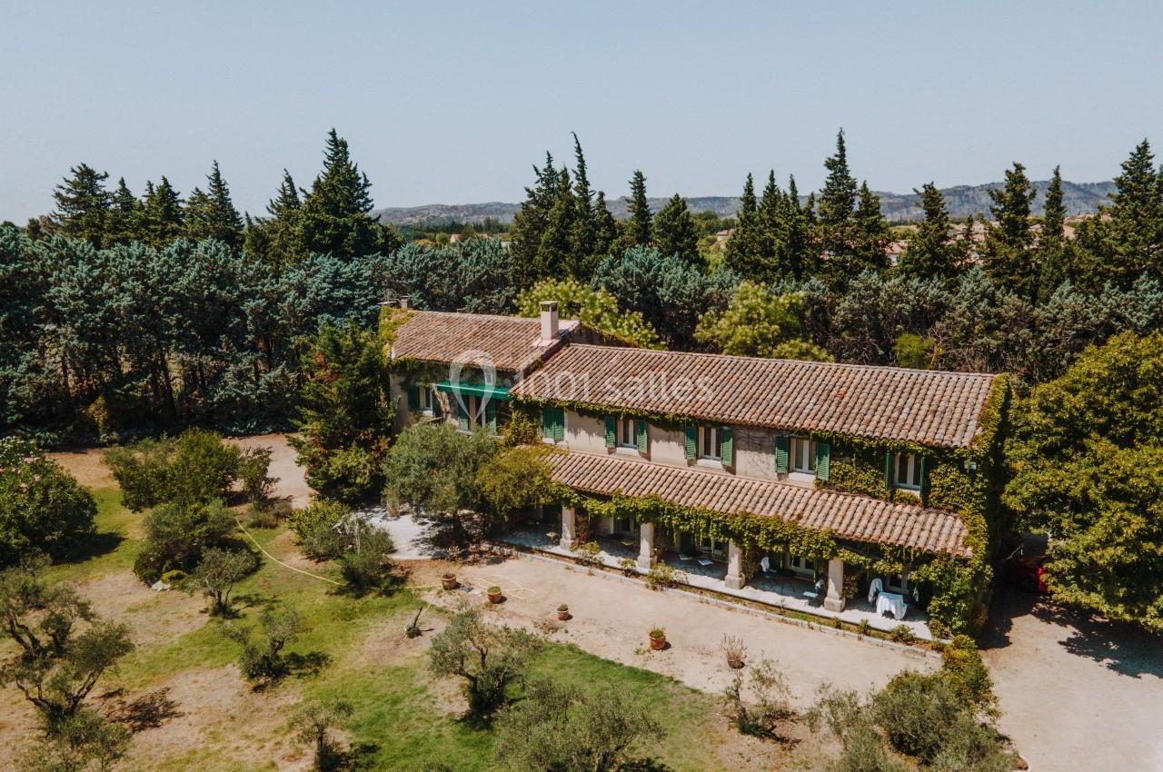 Vue aérienne d'une maison en pierre entourée d'arbres et d'un jardin, sous un ciel clair.