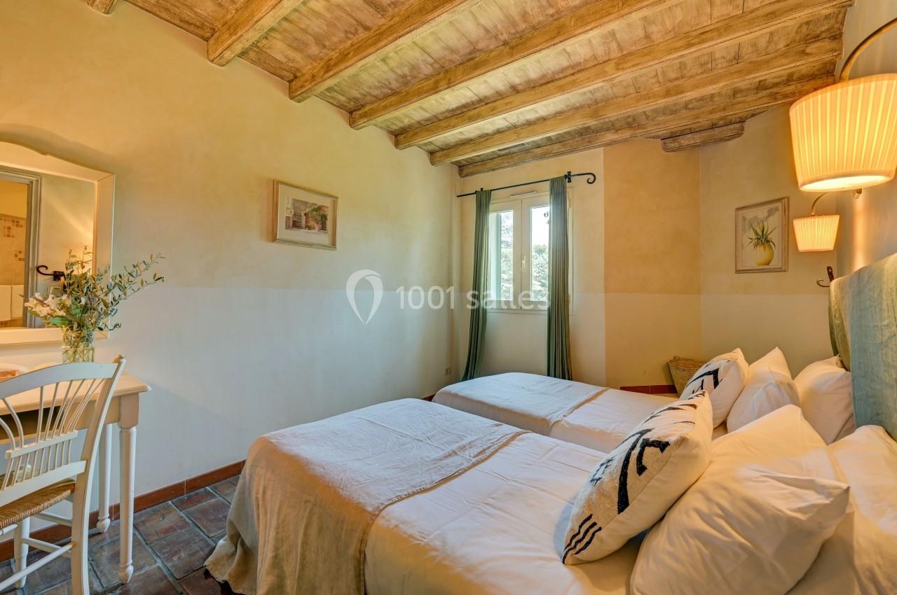 Chambre lumineuse avec deux lits simples, plafond en bois, murs clairs, bureau et fenêtre donnant sur un extérieur verdoyant.