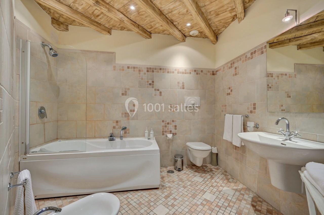 Salle de bain lumineuse avec baignoire, lavabo, toilettes et carrelage beige sous un plafond en bois.