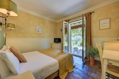 Vue d'une chambre cosy avec lit, éclairage doux, rideaux verts et table extérieure ornée de plantes et d'une tasse.