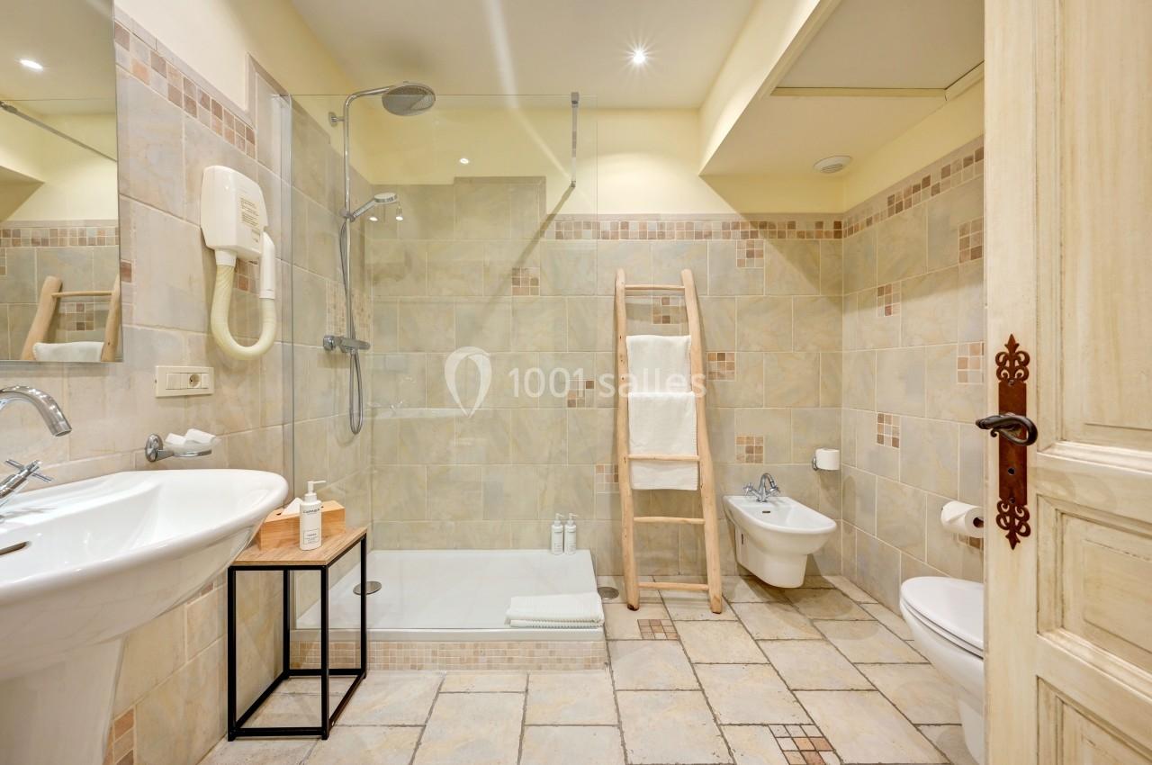 Salle de bain lumineuse avec douche à l'italienne, lavabo, bidet, toilettes et échelle porte-serviettes en bois.