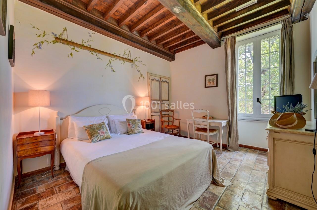 Chambre lumineuse avec lit double, poutres apparentes, bureau près d'une fenêtre et décoration naturelle.