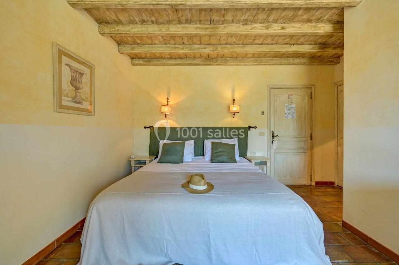 Chambre avec lit double, murs jaunes, plafond en bois, sol en carrelage et chapeau posé sur le lit.