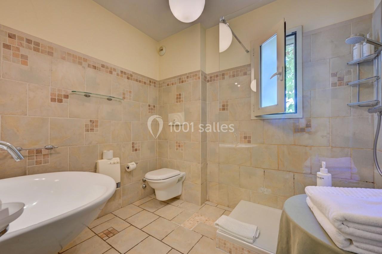 Salle de bain avec douche, lavabo, toilettes suspendues, carrelage beige et fenêtre ouverte sur l'extérieur.