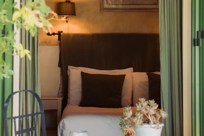 Vue d'une chambre cosy avec lit, éclairage doux, rideaux verts et table extérieure ornée de plantes et d'une tasse.