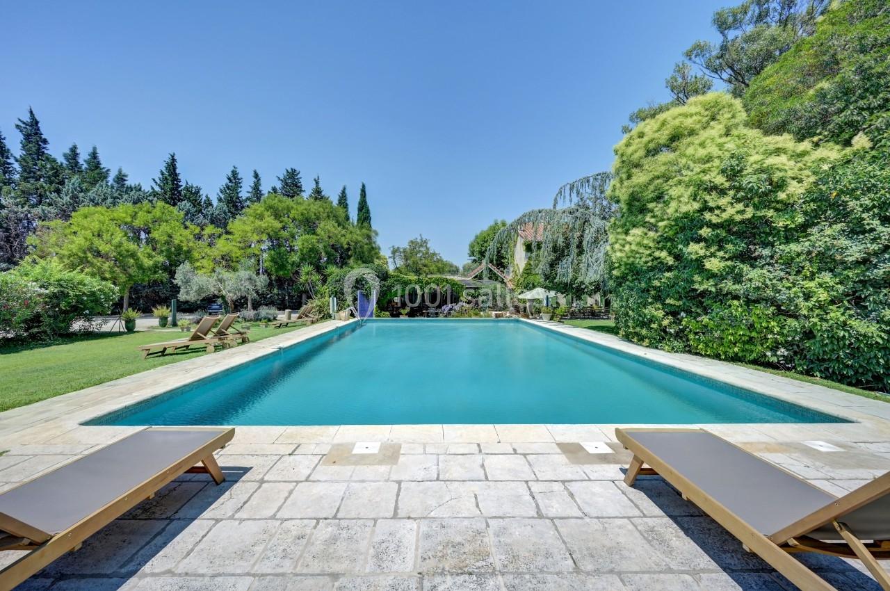 Piscine extérieure entourée de végétation luxuriante, avec transats en bois sur une terrasse en pierre.