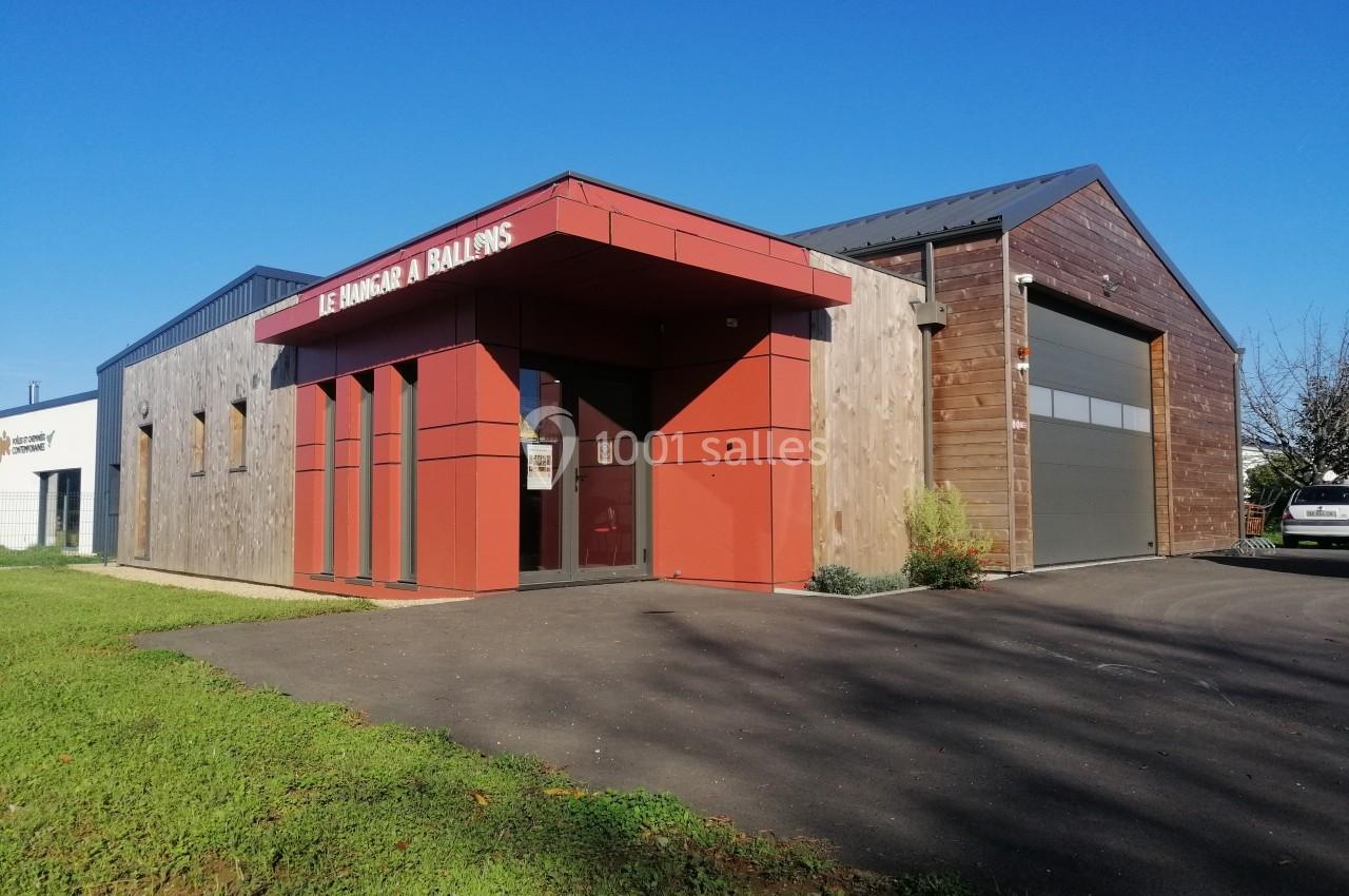 Bâtiment moderne avec façade en bois et rouge, entrée vitrée et grande porte de garage sur la droite.