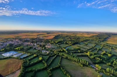 Vue aérienne d'une campagne verdoyante avec champs, haies, étangs et un village sous un ciel bleu dégagé.