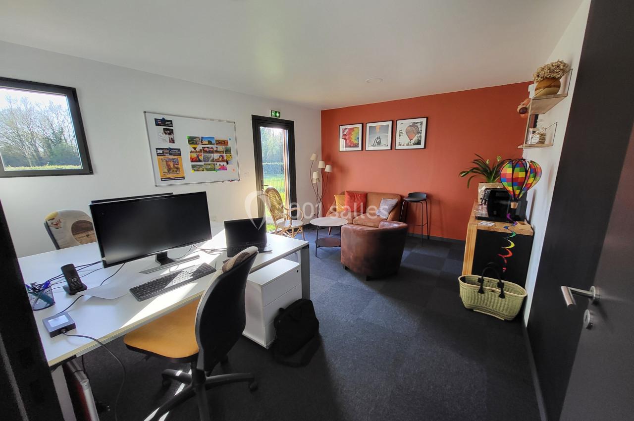 Bureau lumineux avec poste de travail, fauteuils, mur orange décoré et étagères, vue sur l'extérieur.