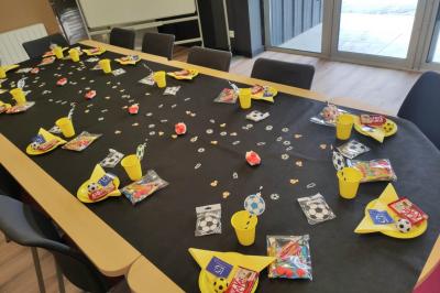 Table décorée pour une fête avec nappes noires, assiettes jaunes, gobelets, bonbons et motifs sur le thème du football.