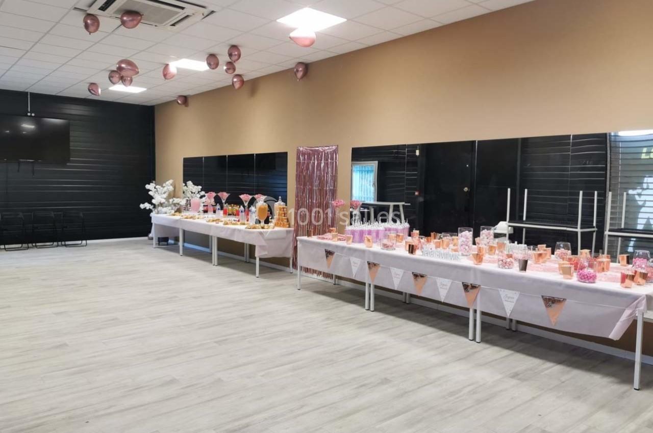 Salle décorée avec des ballons roses et des tables garnies de bonbons et desserts pour un événement festif.