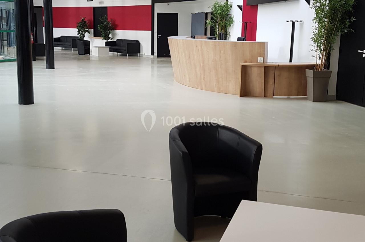 Espace d'accueil moderne avec fauteuils noirs, table basse blanche, comptoir en bois et écrans muraux.