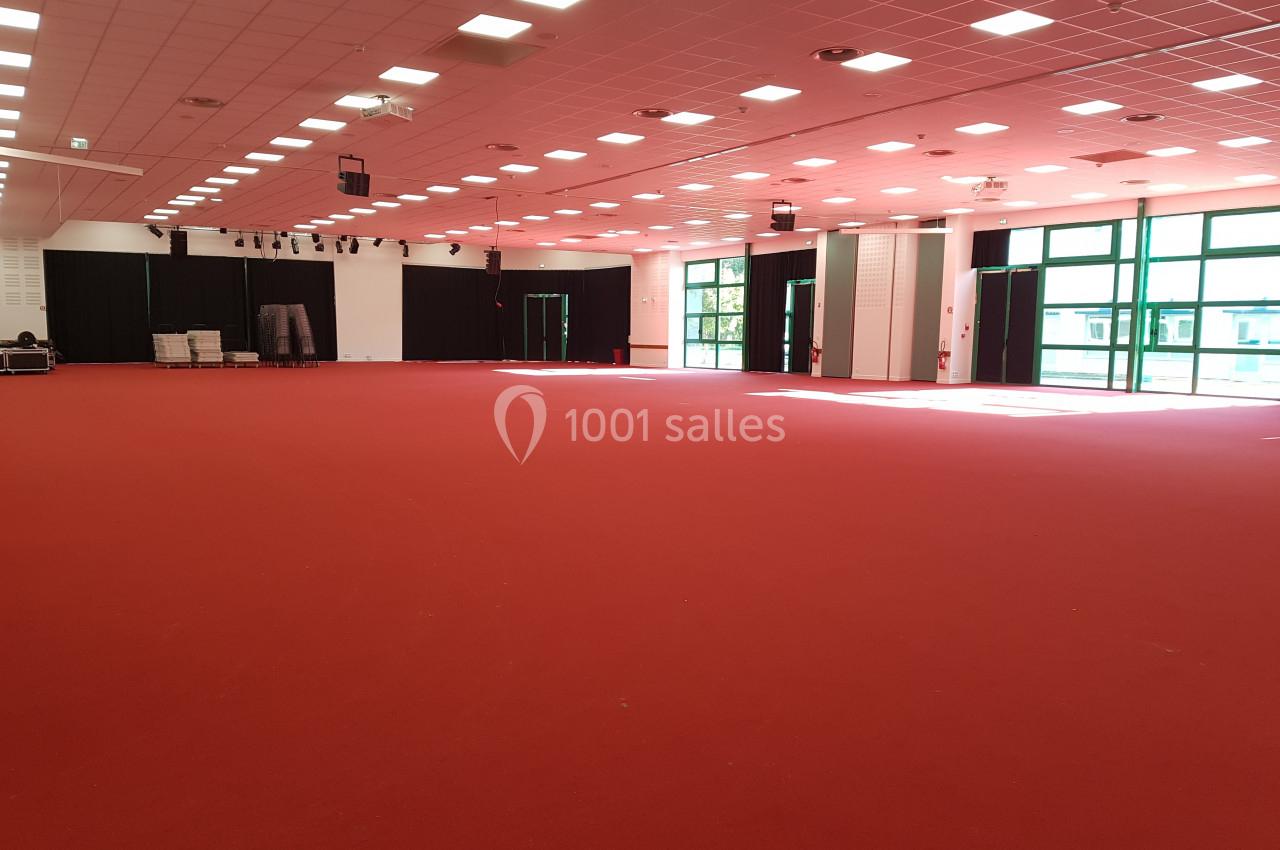 Salle spacieuse avec moquette rouge, éclairée par des fenêtres et des lumières au plafond, équipée de rideaux noirs.