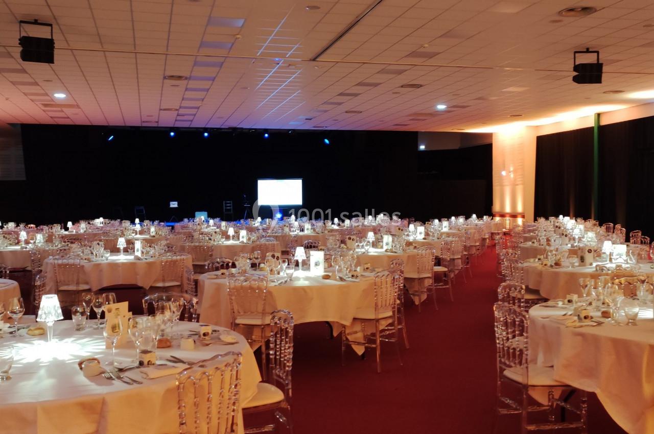 Salle de réception avec tables rondes dressées, chaises transparentes et éclairage tamisé.