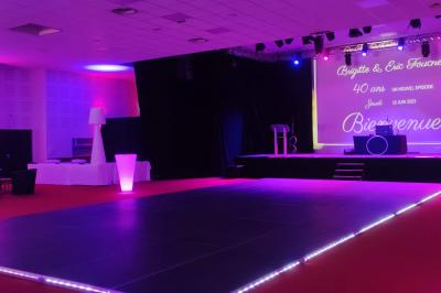 Façade illuminée du bâtiment Auxerrexpo de nuit, avec des visiteurs entrant et deux tracteurs exposés devant.