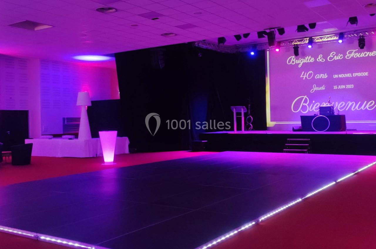 Salle de réception avec piste de danse éclairée, scène équipée et écran affichant un message de bienvenue.