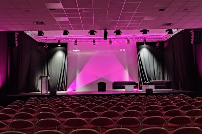 Façade illuminée du bâtiment Auxerrexpo de nuit, avec des visiteurs entrant et deux tracteurs exposés devant.