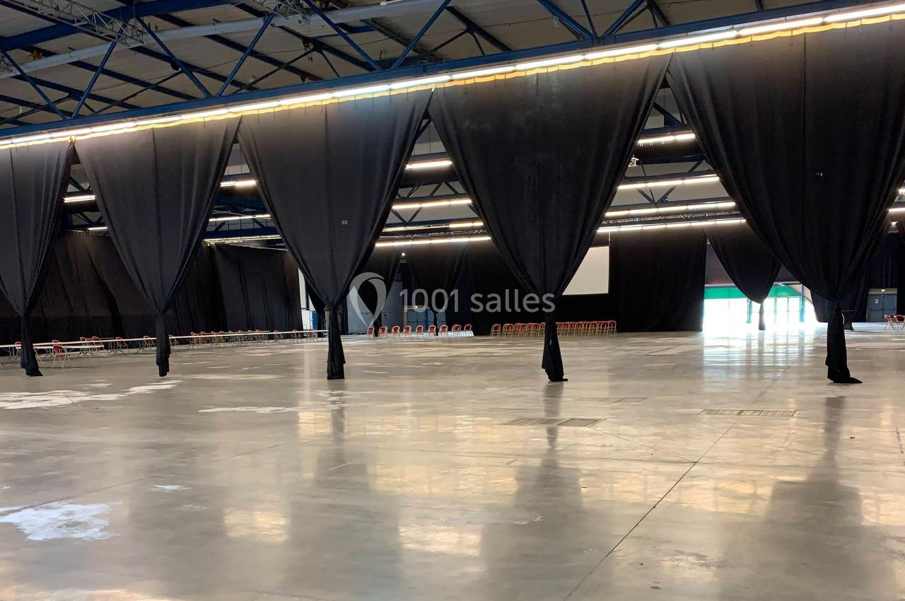 Grand espace intérieur vide avec sol en béton, séparé par de grands rideaux noirs suspendus sous un plafond métallique.