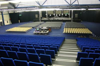 Façade illuminée du bâtiment Auxerrexpo de nuit, avec des visiteurs entrant et deux tracteurs exposés devant.