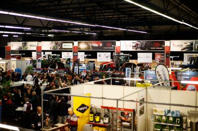 Façade illuminée du bâtiment Auxerrexpo de nuit, avec des visiteurs entrant et deux tracteurs exposés devant.