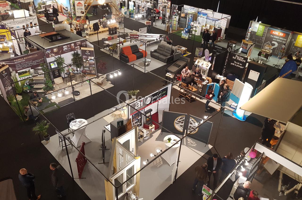 Vue aérienne d'un salon professionnel avec des stands exposant divers produits et services, et des visiteurs circulant.