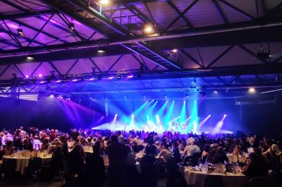 Façade illuminée du bâtiment Auxerrexpo de nuit, avec des visiteurs entrant et deux tracteurs exposés devant.