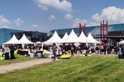 Façade illuminée du bâtiment Auxerrexpo de nuit, avec des visiteurs entrant et deux tracteurs exposés devant.
