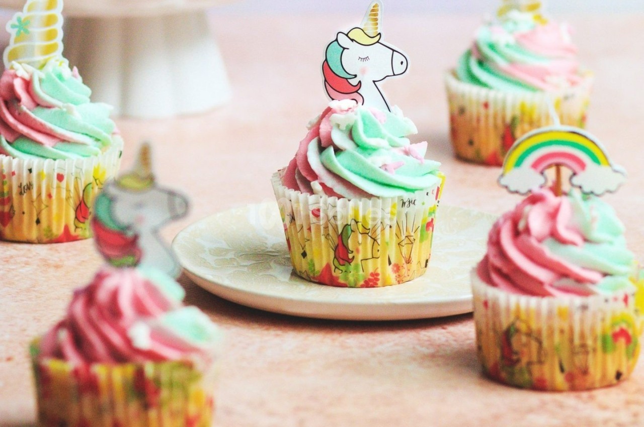 Cupcakes décorés de glaçage rose et vert pastel, ornés de motifs de licornes et d'arcs-en-ciel.