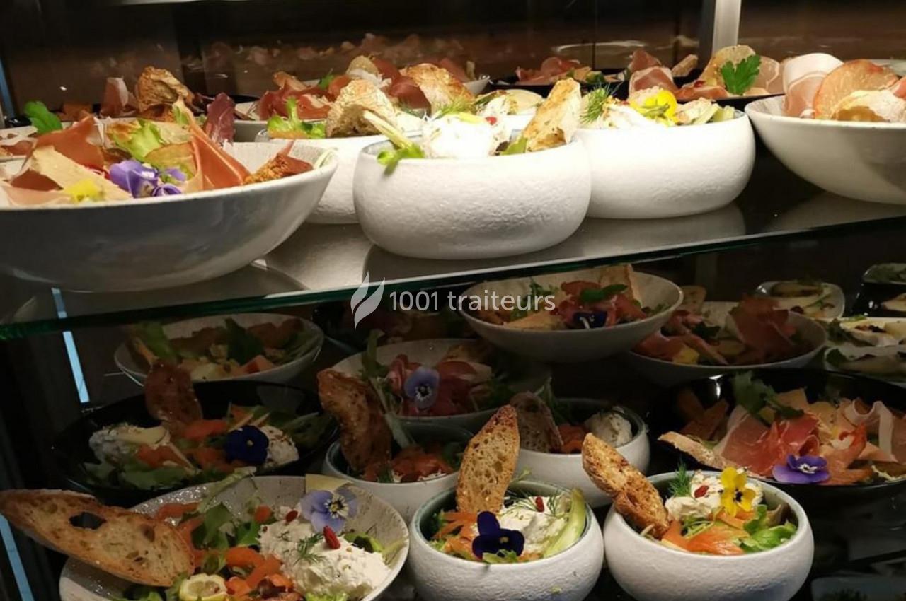 Assortiment de salades garnies de légumes, fleurs comestibles, pain grillé et charcuterie, disposées sur des étagères.