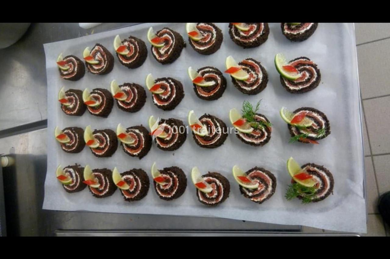 Plateau de bouchées apéritives en spirale garnies de crème, citron, aneth et tomate, disposées sur du papier sulfurisé.