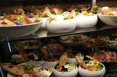 Assortiment de salades garnies de légumes, fleurs comestibles, pain grillé et charcuterie, disposées sur des étagères.