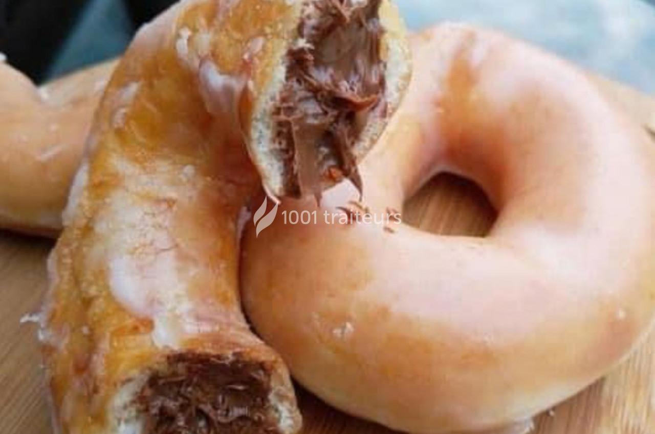 Beignet glacé coupé en deux, révélant une garniture au chocolat, posé sur une surface en bois.